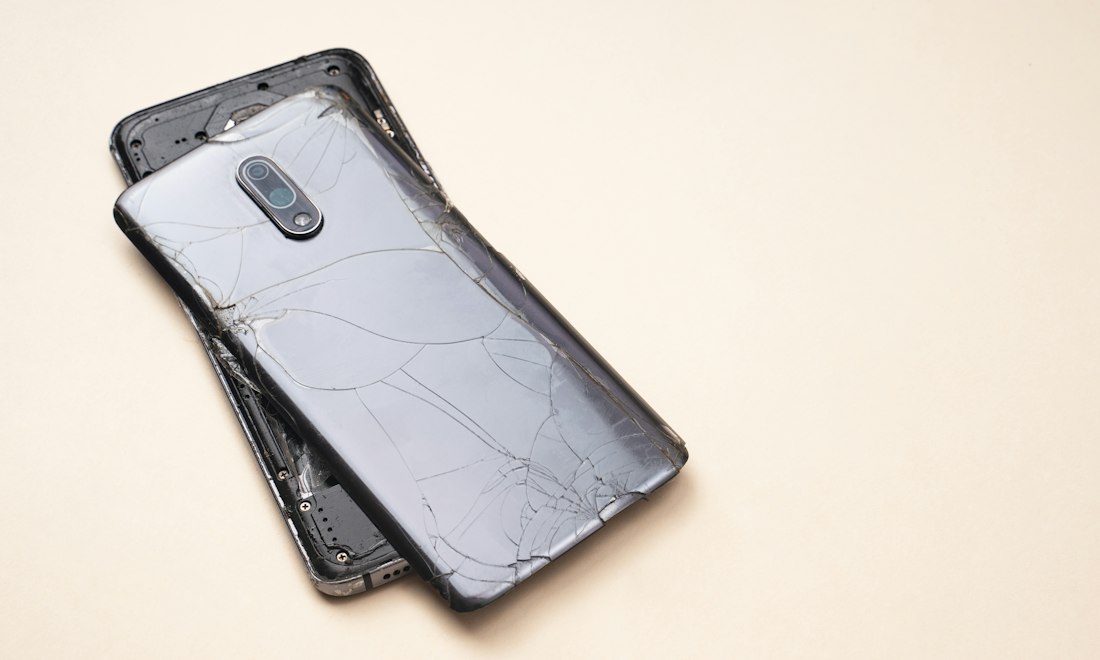 Damaged smartphone with cracked casing on a plain background
